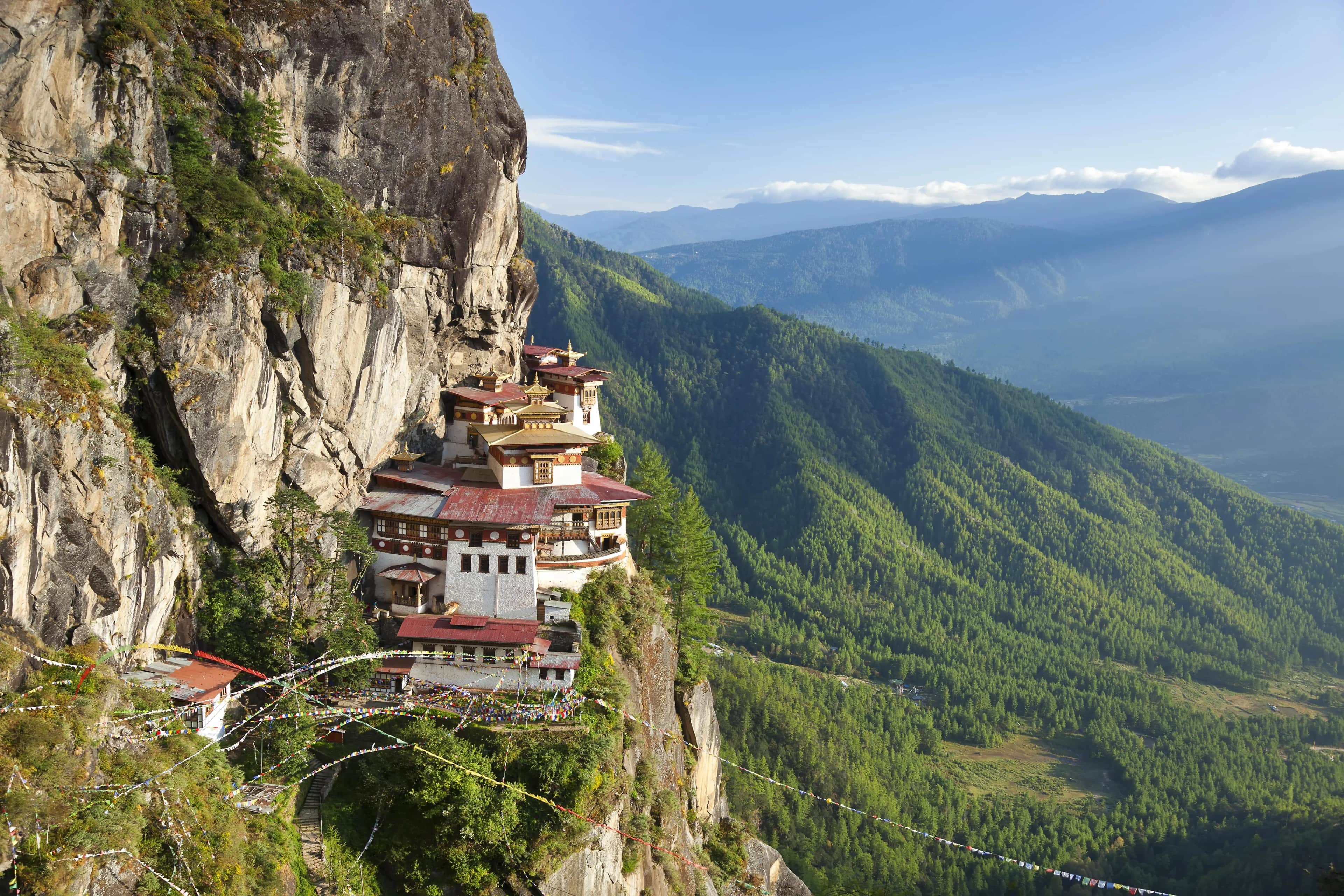 Image for Traditional Bhutanese Buddhist temple complex, Paro Taktsang, built into a granite cliff face with red-roofed buildings and colorful prayer flags in the Himalayan mountains.